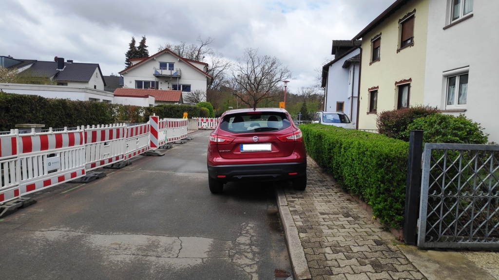 Ein Auto parkt so auf dem Gehweg, dass kein Rollstuhl oder Kinderwagen daran vorbeikommt. 
