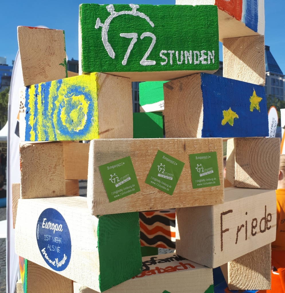 Gestapelte und bemalte Holzbalken, u.a. mit dem Logo der 72 Stunden Aktion. Foto BDKJ Bundesstelle