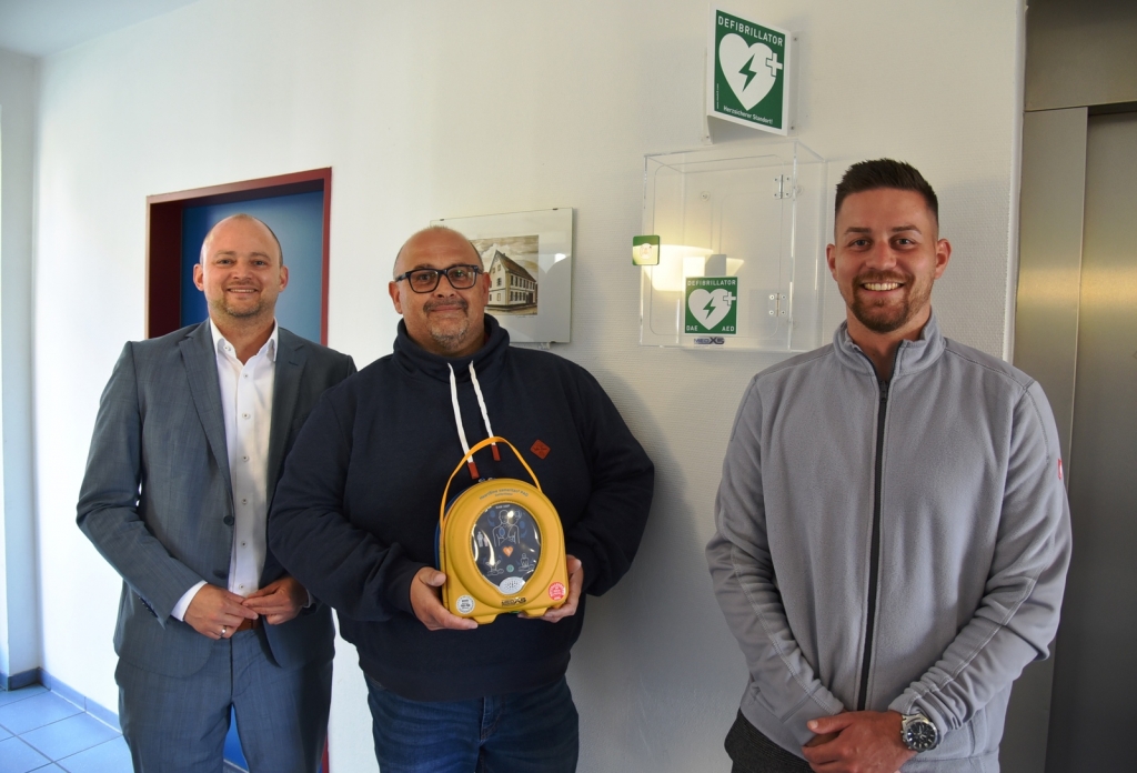 Bürgermeister Pascal Seidel mit Bernd Hertlein und Marcel Pfau vor dem neu installierten Defibrillator im Siegwald-Kehder-Haus.