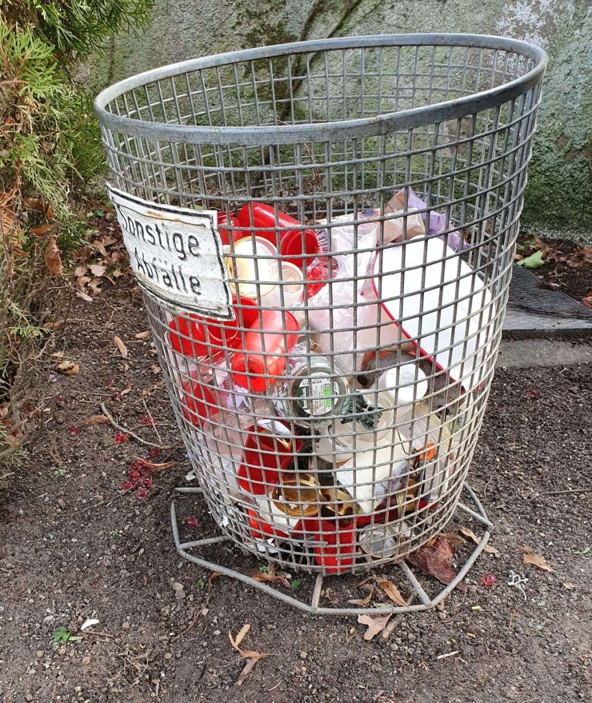 Bild eines Abfalleimers auf dem Oftersheimer Friedhof mit einigen leeren Grablichterhüllen. Foto von Wilmes