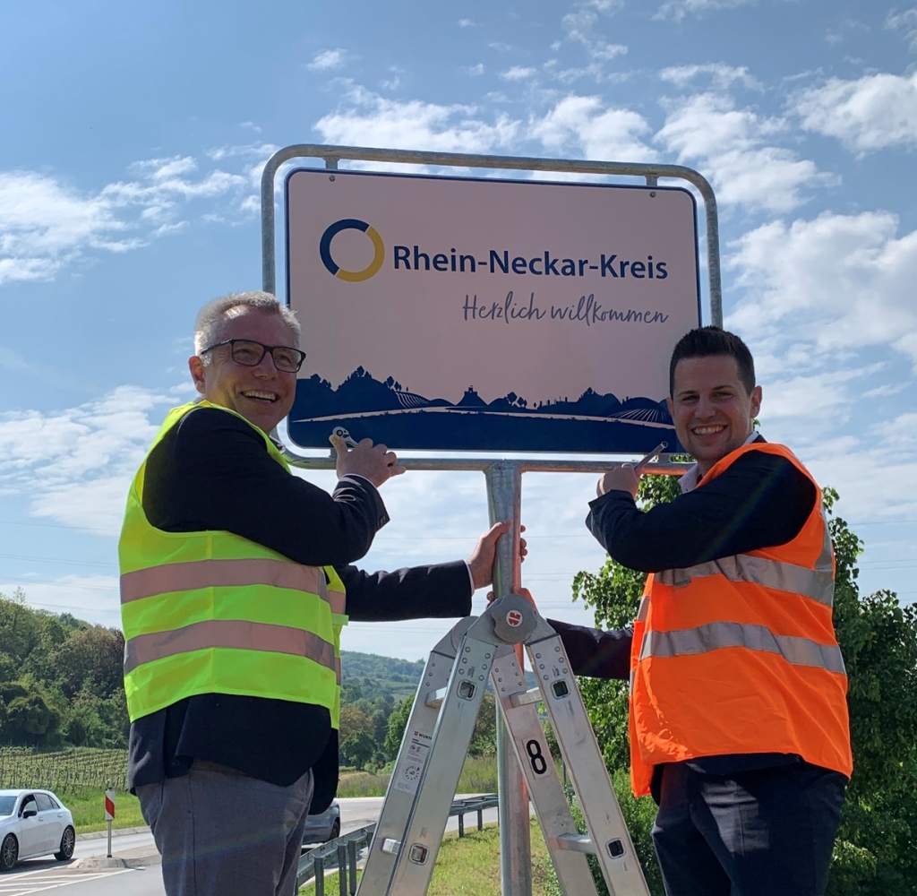 Landrat Stefan Dallinger und Bürgermeister Benjamin Köpfle freuen sich über das erste Willkommensschild im Landkreis. (Bild: Landratsamt Rhein-Neckar-Kreis)