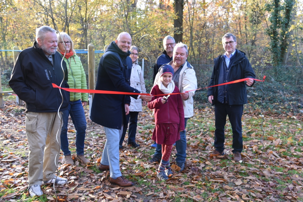 Julia Emilia Habicht schneidet das rote Band für die neuen Spielgeräte durch. Mit dabei sind Vorstandsmitglieder des Gartenbauvereins Oftersheim (Tillmann Hettinger, Martin Halter, Marina Braun und Wolfgang Schifferdecker) und Bürgermeister Pascal Seidel sowie Bauhofleiter Jochen Barisch mit seiner Mitarbeiterin Simone Orians.