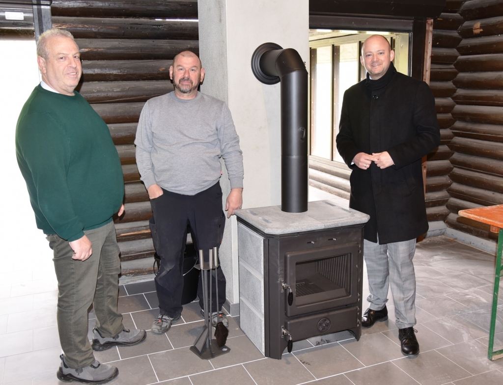 Die Hausmeister Harald Gruber und Jürgen Sturm stehen mit Bürgermeister Pascal Seidel neben dem neuen Kaminofen.